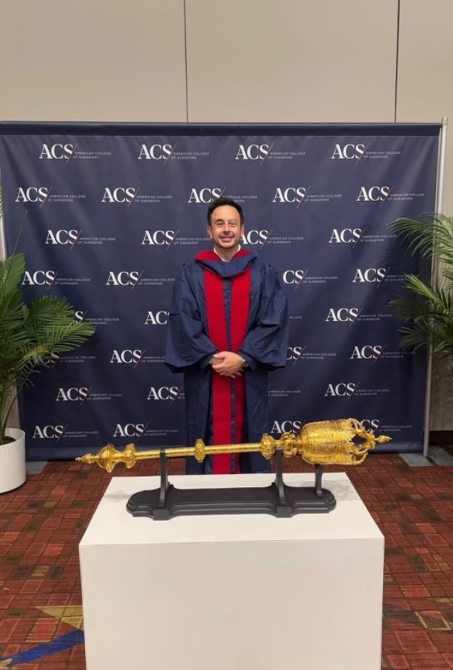 A person in academic regalia stands in front of an ACS backdrop, behind a table displaying an ornate gold ceremonial mace.